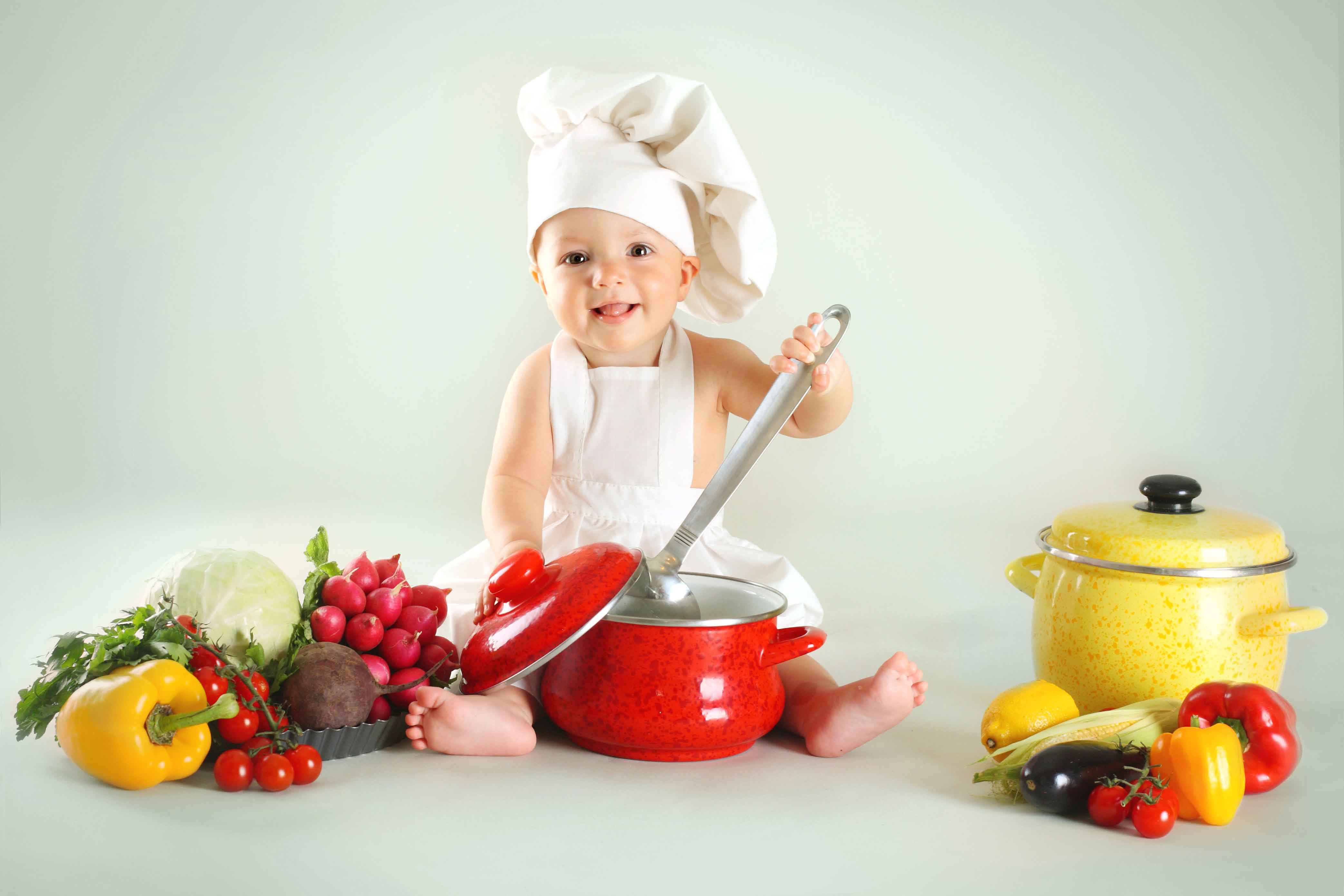 Baby wearing a chef hat with vegetables and pan